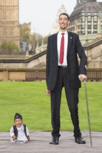 Sultan Kösen, born on December 10, 1982, is a Turkish farmer who holds the prestigious Guinness World Record for being the tallest living male, standing at a remarkable 251 cm (8 feet 2.82 inches). Sultan Kösen Kösen’s extraordinary growth was a result of two medical conditions, gigantism and acromegaly, stemming from a tumor that affected his pituitary gland. Due to his condition, he relies on crutches to assist him in walking. Biography: Kösen, an individual of Turkish and ethnic Kurdish heritage, was born in the village of Alibey in the Mardin Province of Turkey. Unfortunately, due to his exceptional height, Kösen couldn’t complete his formal education and instead worked part-time as a farmer. He acknowledges the advantages of being tall, such as having an extended field of vision and being able to assist his family with everyday tasks like changing light bulbs and hanging curtains. Nevertheless, he also encounters disadvantages, including the difficulty of finding clothes that fit his 126 cm (49.61 inches) long legs, or shirts that accommodate his 97 cm (38.19 inches) long arms, and shoes for his once record-breaking foot length of 36.5 cm (14.4 inches) on the left and 35.5 cm (14.0 inches) on the right. Furthermore, his hands hold the record as the longest measured in a living person at 28.5 cm (11.2 inches). He even struggles to fit into an average-sized car. Starting in 2010, Kösen underwent Gamma Knife treatment for the pituitary tumor at the University of Virginia Medical School and received medication to control his excessive growth hormone levels. It was confirmed in March 2012 that this treatment successfully halted Kösen’s continuous growth. In October 2013, Kösen married Merve Dibo, a Syrian-born woman ten years his junior. In interviews, he expressed that one of their major challenges was communication, as he spoke Turkish while his wife only spoke Arabic. In 2021, they divorced, citing the language barrier as a significant issue. Kösen maintains the hope of finding a new partner in the future. On November 13, 2014, as part of Guinness World Records Day, Kösen had his first encounter with the world’s shortest man ever, Chandra Bahadur Dangi, whose height measured at 54.6 cm (1 foot 9+1⁄2 inches). The height disparity between them was a remarkable 196.4 cm (6 feet 5.32 inches). In 2014, Kösen became a part of the Magic Circus of Samoa and participated in various shows across the globe. Kösen celebrated his 40th birthday a few days early, on December 10, 2022, by visiting the Ripley’s Believe It or Not! museum in Orlando, Florida, United States. There, he posed next to a life-sized statue of Robert Wadlow, the tallest man ever, whose height was 272 cm (8 feet 11.1 inches). Records: On August 25, 2009, Kösen’s standing height was officially recorded at 246.4 cm (8 feet 1 inch) in his home country by Guinness World Records, surpassing the former world record holder, Bao Xishun, who stood at 236.1 cm (7 feet 8+15⁄16 inches). Kösen also holds the current Guinness record for the largest hands, measuring 27.5 cm (10+7⁄8 inches), and the second-largest feet: 36.5 cm (14+3⁄8 inches) for the left foot and 35.5 cm (14 inches) for the right foot. On August 25, 2010, the University of Virginia confirmed a height of up to 254.3 cm (8 feet 4+1⁄8 inches) after doctors reevaluated him. They suggested that this might be Kösen’s actual height, artificially lowered by scoliosis and poor posture. On February 9, 2011, Guinness World Records conducted another measurement, recording Kösen’s height at 251 cm (8 feet 2+7⁄8 inches). They also reconfirmed his hands’ measurements at 28 cm (11 inches), breaking his previous record. Back to the tallest people ever. 
